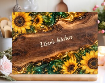 Peut inclure: Une planche à découper rectangulaire avec un panneau central en bois foncé portant l'inscription Elize's kitchen en écriture blanche. Elle est bordée de tournesols jaunes, de feuilles vertes et de résine dorée et vert émeraude tourbillonnante.