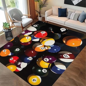 May include: A rectangular area rug featuring a design of colorful billiard balls against a black background. The balls are numbered and include various colors such as red, yellow, blue, and purple. The rug is placed on a wooden floor.