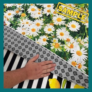 May include: A black and white striped rug with a white daisy pattern on the top. The rug has a black and white checkered backing. The word "SAMPLE" is printed in yellow on a black rectangle.