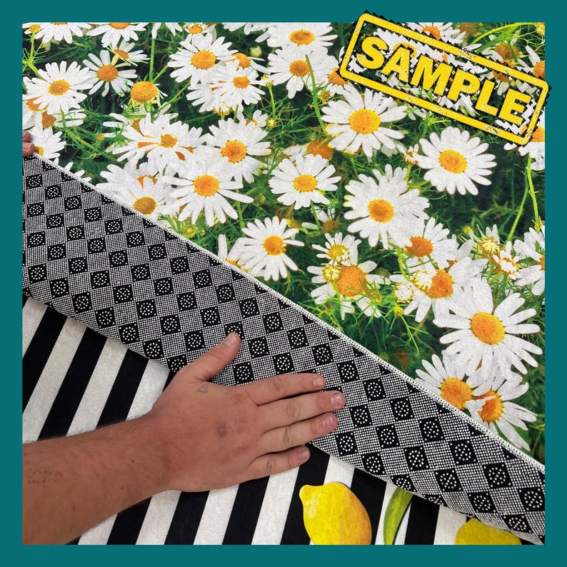 May include: A black and white striped rug with a white daisy pattern on the top. The rug has a black and white checkered backing. The word "SAMPLE" is printed in yellow on a black rectangle.