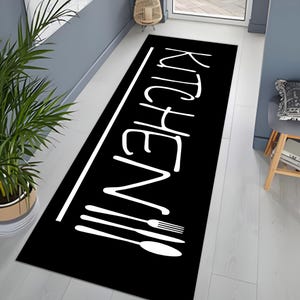 May include: Black and white kitchen rug with the word "Kitchen" written in a stylised font. The rug also features a row of white silhouettes of kitchen utensils.