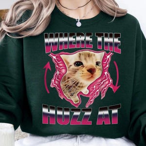 Op de afbeelding: Een witte keramische mok met een zwarte handgreep en de tekst "But First, Coffee" in een vetgedrukte, zwarte letter. De mok staat tegen een vage achtergrond. De mok is ongeveer 10 cm hoog.