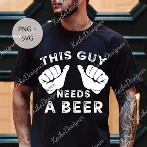 May include: Black t-shirt with the text "THIS GUY NEEDS A BEER" in white, along with two white hand illustrations. The shirt design is a humorous statement.