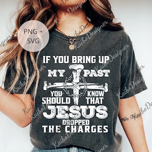 May include: Dark gray t-shirt with white text and a graphic of a cross, nails, and a crown of thorns. The text reads "IF YOU BRING UP MY PAST YOU SHOULD KNOW THAT JESUS DROPPED THE CHARGES."