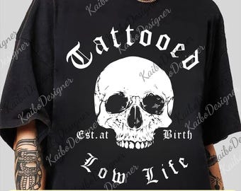 May include: Black t-shirt with a white skull graphic. The skull is centered and has the words "Tattooed" above it, and "Est. at Birth, Low Life" below. The bottom of the image has the text "PNG + SVG".