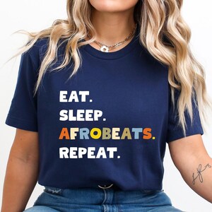 May include: A navy blue t-shirt with the text "Eat. Sleep. AfroBeats. Repeat." in colorful letters.