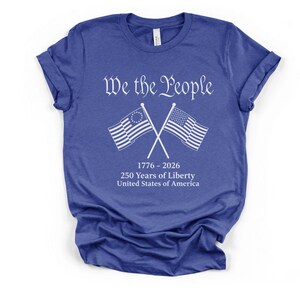 May include: Blue t-shirt with the text "We the People" in white script above crossed American flags. Below the flags is the text "1776-2026 250 Years of Liberty United States of America."