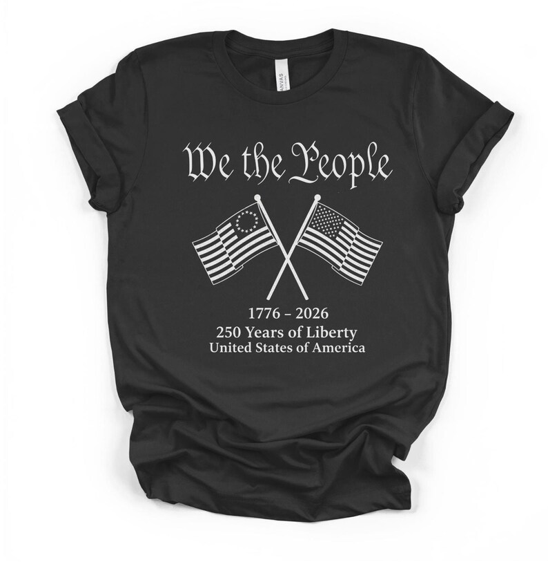 May include: Black t-shirt with the text "We the People" in a decorative font. Below the text are two crossed flags, one with a circle of stars and the other with stripes. The shirt also includes the text "1776-2026 250 Years of Liberty United States of America."
