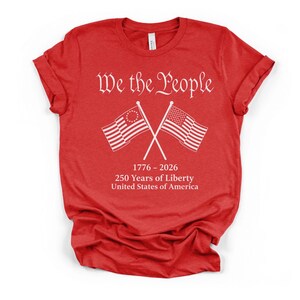 May include: A red t-shirt with white text and graphics. The text reads "We the People" above crossed American flags. Below the flags is "1776 - 2026 250 Years of Liberty United States of America."