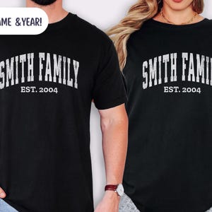 May include: Black t-shirts with the text "SMITH FAMILY EST. 2004" in a distressed white font. The shirts are short-sleeved and appear to be made of a soft material. The image shows two people wearing the shirts.
