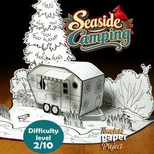 Op de afbeelding: Een papieren knutselset met een zwart-witte caravan, bomen en vogels. De tekst luidt Seaside Camping en Timeless Paper Project, met een blauwgroene cirkel Difficulty level 2/10. Het ontwerp bevat bloemmotieven op de caravan.