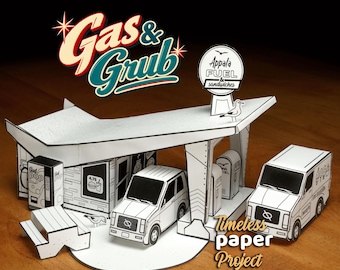May include: A paper craft model of a gas station and convenience store featuring a white roof, black and white printed details, a soda machine, a picnic table, two vehicles, and a sign that reads Appala FUEL & sandwiches.