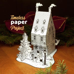 May include: A black and white paper craft set featuring a tall house with two chimneys, a decorated tree, and figures building a snowman. The text Timeless paper Project is printed on the left. The structure is made of white paper with black line art details.