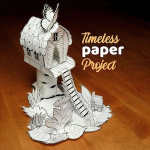 May include: A white paper craft structure featuring a small house with a butterfly on the roof, a ladder, and a base decorated with leaves and flowers. The text Timeless paper Project is printed in orange next to the paper house model.