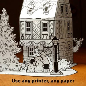 May include: A black and white paper craft set featuring a two-story house with a gabled roof, a decorated Christmas tree, a street lamp, and figures building a snowman. The text "Use any printer, any paper" is printed at the bottom.