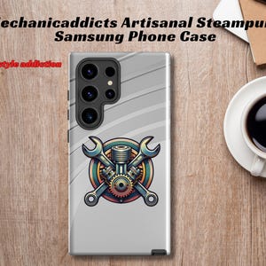 以下が含まれることがあります： グレーのサムスン携帯電話ケースで、スチームパンクのデザインが施されています。2本のレンチがギアとエンジンを交差して配置されています。画像の上部には「Mechanicaddicts Artisanal Steampunk Samsung Phone Case」というテキストが書かれています。画像の下部には「It's a lifestyle addiction」というテキストが書かれています。