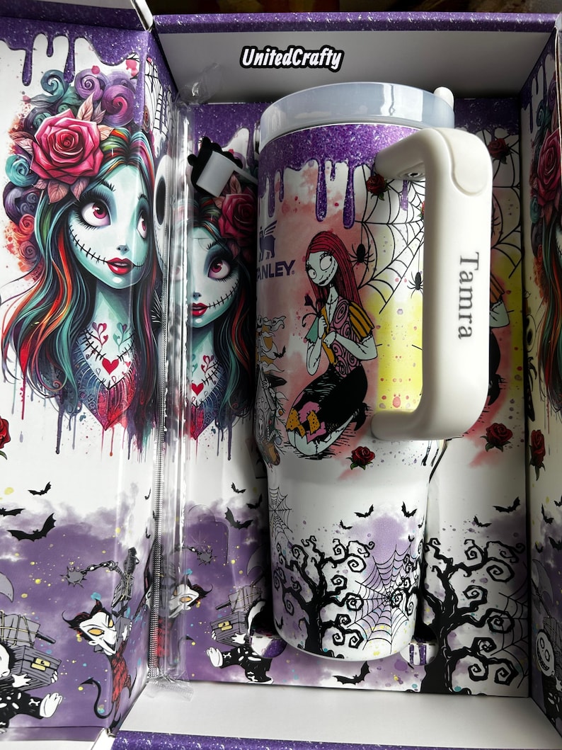 Puede incluir: Un vaso blanco con asa, con una colorida ilustraci&oacute;n de un personaje con puntadas y rosas, junto con una caja a juego. La caja y el vaso tienen un tema de Halloween con murci&eacute;lagos, telara&ntilde;as y &aacute;rboles. El asa tiene el nombre "Tamra".