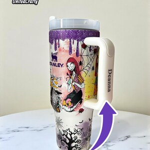 Puede incluir: Un vaso Stanley personalizado con un dise&ntilde;o de Sally de Pesadilla antes de Navidad. El vaso tiene un asa blanca con el nombre "Deanna" y las palabras "Custom Name" en la parte inferior. El borde superior es morado con purpurina.