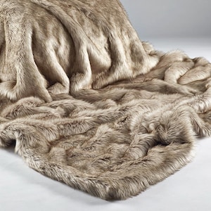 May include: A luxurious faux fur throw blanket in shades of brown and beige. The blanket is draped, displaying its soft texture and opulent appearance. The faux fur has long, flowing fibres, creating a cosy look.