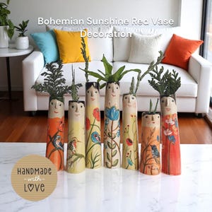 Könnte beinhalten: Sieben handbemalte Keramikvasen mit Gesichtern und Blumenmustern. Die Vasen sind in Orange, Gelb und Creme gehalten, mit grünem Laub. Der Text "Bohemian Sunshine Red Vase Decoration" steht oben. Dekorative Wohnkultur.