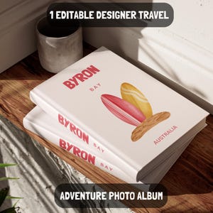 Pode incluir: Álbum de fotos branco com as palavras "BYRON BAY" em vermelho. A capa apresenta ilustrações de pranchas de surf e a palavra "AUSTRALIA". Os textos "1 EDITABLE DESIGNER TRAVEL" e "ADVENTURE PHOTO ALBUM" também são visíveis.