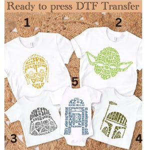 Puede incluir: Cuatro camisetas blancas con diferentes diseños de personajes de Star Wars. Los diseños están hechos de palabras relacionadas con los personajes. Los diseños son en oro, verde, gris y azul.