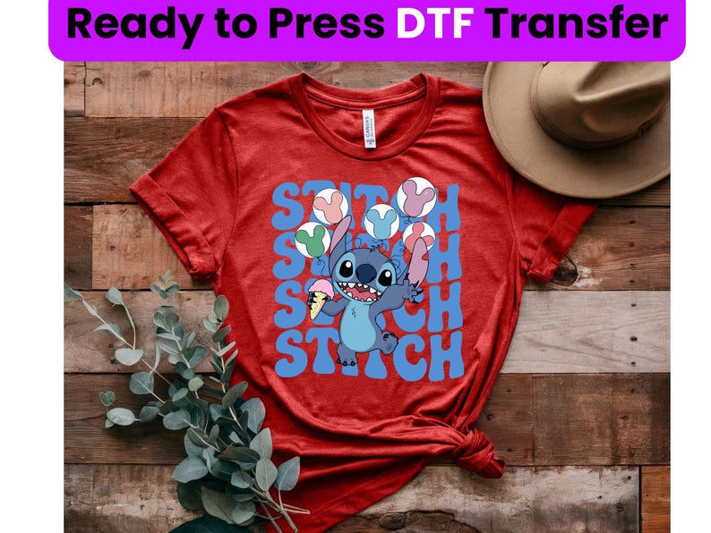 Puede incluir: Camiseta roja con un personaje azul Stitch sosteniendo un cono de helado. La camiseta tiene el texto "Stitch" escrito en letras azules.