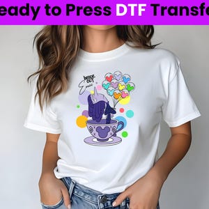 以下が含まれることがあります： 白いTシャツに、ティーカップと風船を持った紫色のキャラクターのグラフィックがプリントされています。風船には「Inside Out」と書かれています。