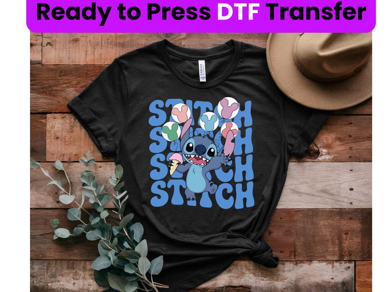 Puede incluir: Camiseta negra con un personaje azul Stitch sosteniendo un cono de helado y rodeado de globos de colores. El texto "Stitch" est&aacute; escrito en letras azules en la camiseta.