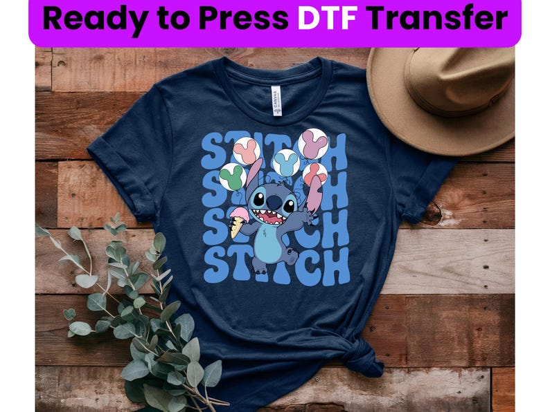 Puede incluir: Una camiseta azul marino con un gr&aacute;fico de Stitch de Lilo & Stitch sosteniendo un helado y haciendo malabares con orejas de Mickey Mouse. El texto "Stitch" se repite en una fuente retro.