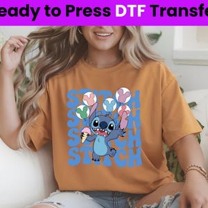 Puede incluir: Una mujer lleva una camiseta amarilla mostaza con un gr&aacute;fico azul de Stitch y el texto "Stitch" repetido en azul. El gr&aacute;fico muestra a Stitch sosteniendo un cono de helado rosa y blanco y rodeado de globos de colores.