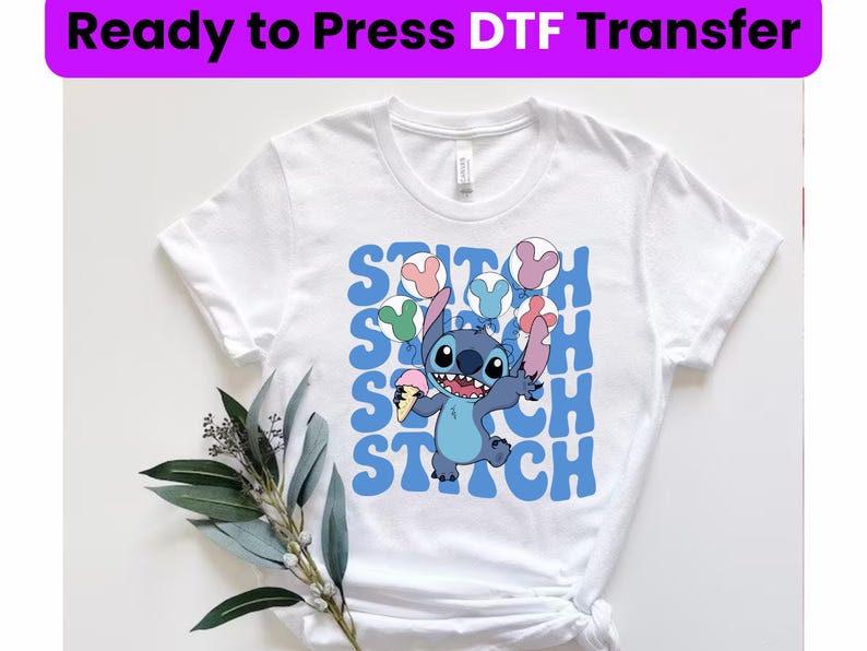 Puede incluir: Camiseta blanca con un gr&aacute;fico azul y blanco de Stitch de Lilo & Stitch sosteniendo un cono de helado azul y globos. El texto "Stitch" se repite en una fuente retro azul.