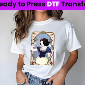 以下が含まれることがあります： 白地に、ヴィンテージフレームの中にスノウホワイトのグラフィックプリントが施されたTシャツ。グラフィックは、スノウホワイトが手に鳥を持ち、背景に赤いリンゴが描かれている。画像の上部には「Ready to Press DTF Transfer」というテキストが書かれている。