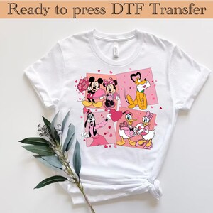 May include: White t-shirt featuring a colorful graphic of Disney characters Mickey, Minnie, Pluto, Goofy, Donald, and Daisy in a Valentine's Day theme. The shirt has the text "Ready to press DTF Transfer" at the top.