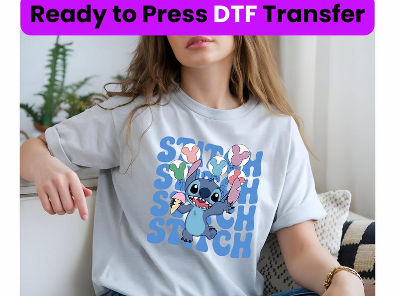 Puede incluir: Una camiseta azul claro con un estampado gr&aacute;fico de Stitch de Lilo & Stitch sosteniendo un cono de helado. El gr&aacute;fico est&aacute; rodeado por la palabra "Stitch" repetida en una fuente retro colorida.