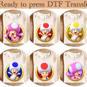 Może przedstawiać: Sześć białych koszulek z nadrukowanymi na nich różnokolorowymi postaciami grzybów. Postacie noszą różnokolorowe stroje. Koszulki są ponumerowane od 1 do 6.