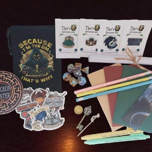 May include: A collection of tabletop role-playing game accessories, including dice, pencils, stickers, and booklets. The set features a notebook with the text "BECAUSE I'M THE DM THAT'S WHY" and a "DUNGEON MASTER" coaster.