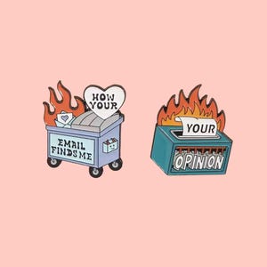 May include: Two enamel pins on a pink background. One pin depicts a blue trash bin on fire with the text "EMAIL FINDS ME" and a heart-shaped sign that says "HOW YOUR". The other pin shows a blue box on fire with the text "YOUR OPINION".
