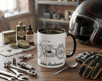 May include: A white coffee mug with a black rim and handle, featuring a vintage motorcycle illustration and the name "John Anderson." The mug sits on a wooden surface with motorcycle tools, lubricants, and a helmet.