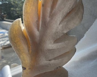 Puede incluir: Una escultura tallada en blanco roto que se asemeja a una pluma o una hoja estilizada. La escultura tiene una superficie lisa y pulida con sutiles variaciones de color, que van del blanco crema al amarillo pálido. El diseño presenta múltiples segmentos alargados.