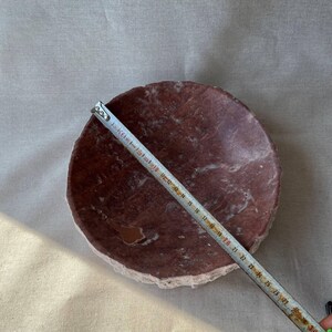 Puede incluir: Un cuenco redondo de piedra marr&oacute;n rojizo con un borde &aacute;spero de color claro. Una cinta m&eacute;trica muestra el di&aacute;metro del cuenco. El di&aacute;metro del cuenco es de aproximadamente 28 cm.