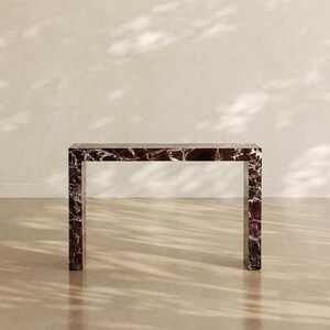 May include: A rectangular console table constructed from dark burgundy marble with prominent white veining. The piece features a clean, linear design with a flat top surface supported by two vertical side panels, creating a simple frame structure.