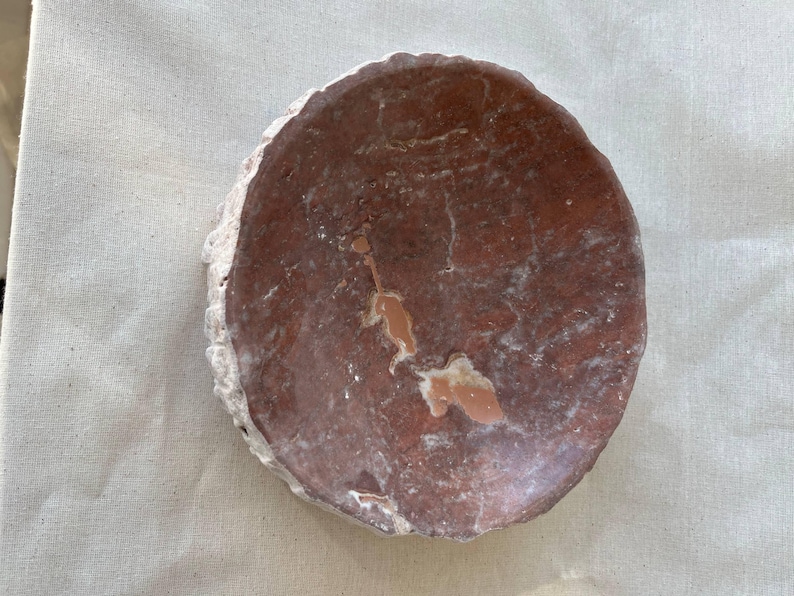 Puede incluir: Una losa de piedra redonda, de color marr&oacute;n rojizo, con un borde blanco rugoso. La superficie tiene un aspecto texturizado con vetas y manchas de color m&aacute;s claro. La piedra est&aacute; sobre un fondo neutro, blanquecino.