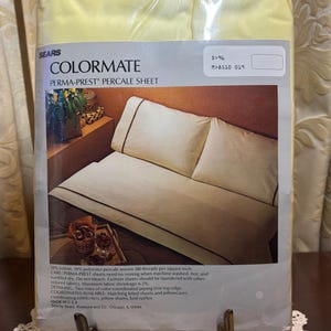 May include: A packaged yellow Sears Colormate Perma-Prest Percale Sheet set. The packaging displays a cream-colored bed with brown trim on the sheets and pillowcases. The packaging also includes the text "COLORMATE PERMA-PREST PERCALE SHEET".