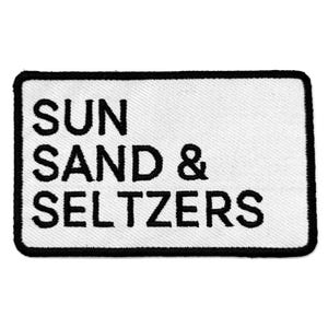 May include: Rectangular white patch with black border. The patch features the words "SUN SAND & SELTZERS" in bold, black capital letters. The patch is likely an accessory.