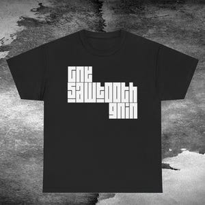 May include: Black t-shirt with the white text "ONE SAWTOOTH GANG" in a unique, blocky font. The shirt is a crew neck style and is displayed against a textured, grayscale background.