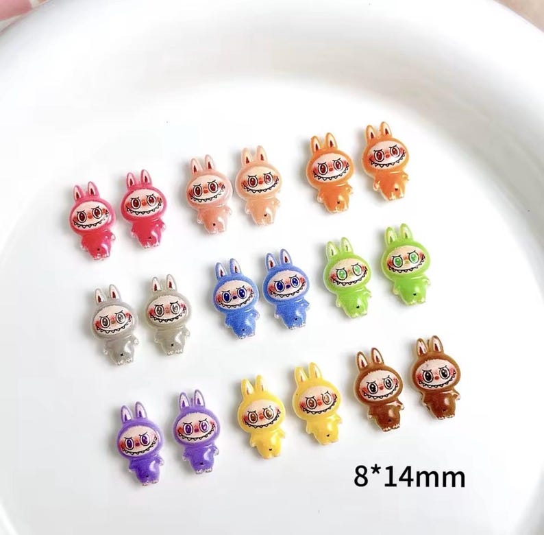 May include: A collection of colorful, cartoonish bunny charms. Each charm is approximately 0.3 x 0.6 inches and features a smiling face and bunny ears. The charms are in various colors, including red, orange, pink, blue, green, yellow, gray, brown, and purple.