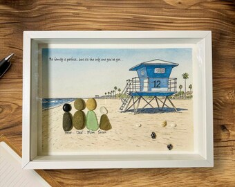 May include: Framed artwork featuring a beach scene with a blue lifeguard tower and palm trees. Pebble art depicts a family of four. Text reads "No family is perfect... but it's the only one you've got." and names the family members.