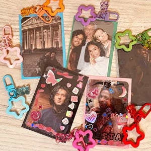 May include: A set of six colorful star-shaped keychains with different images and designs. The keychains feature a variety of themes, including a cityscape, a group of people, and a person with a sticker design.