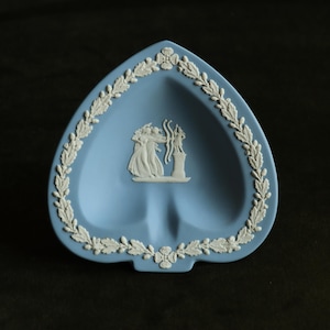 Puede incluir: Un plato de cerámica azul y blanco con forma de corazón con un diseño floral blanco alrededor del borde. El centro del plato presenta un diseño blanco de tres figuras.
